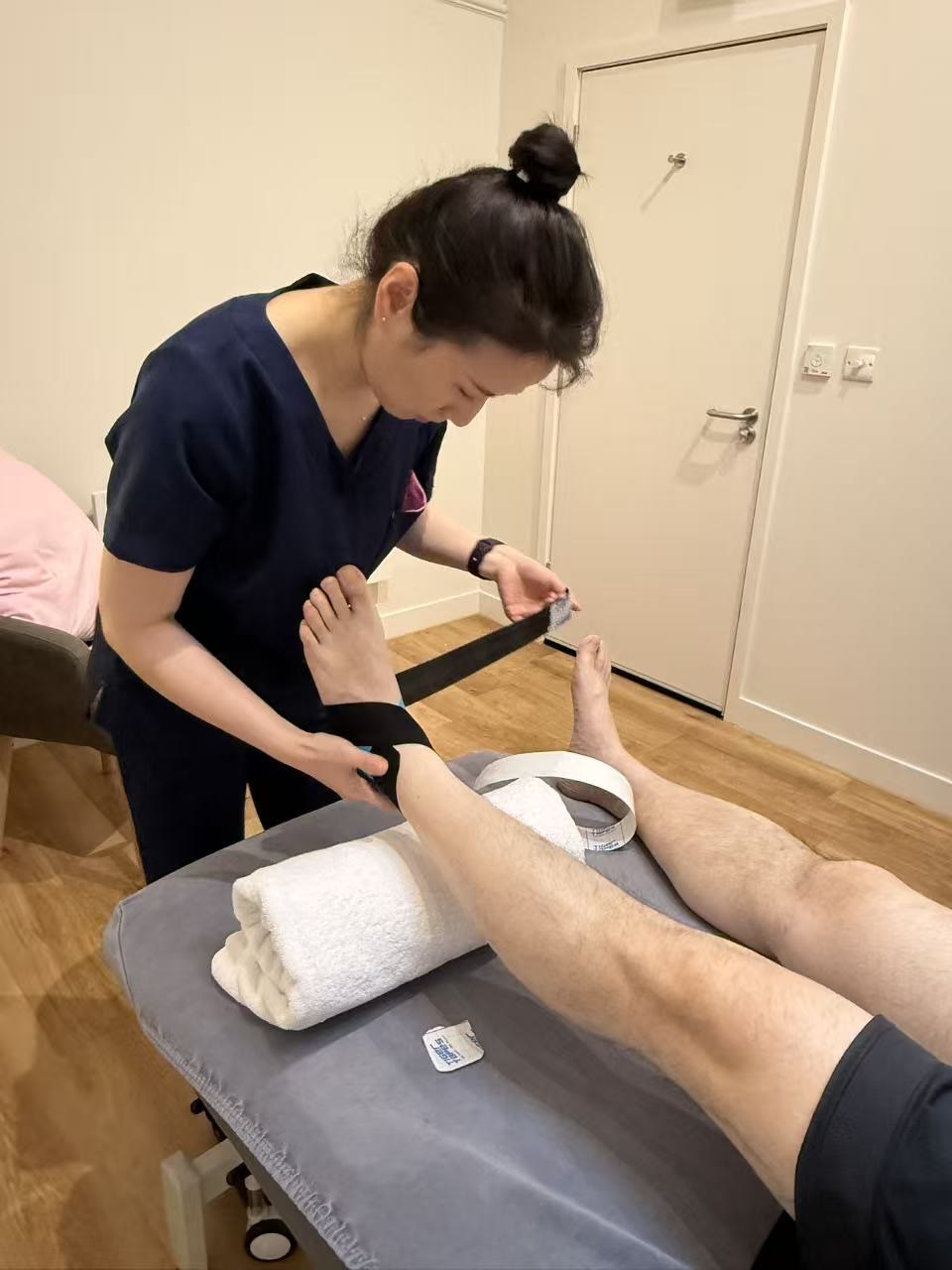 Yan Liu applying sports tape to a patient’s sprained ankle on the treatment couch at Rehab Joy, 113 Kingsway